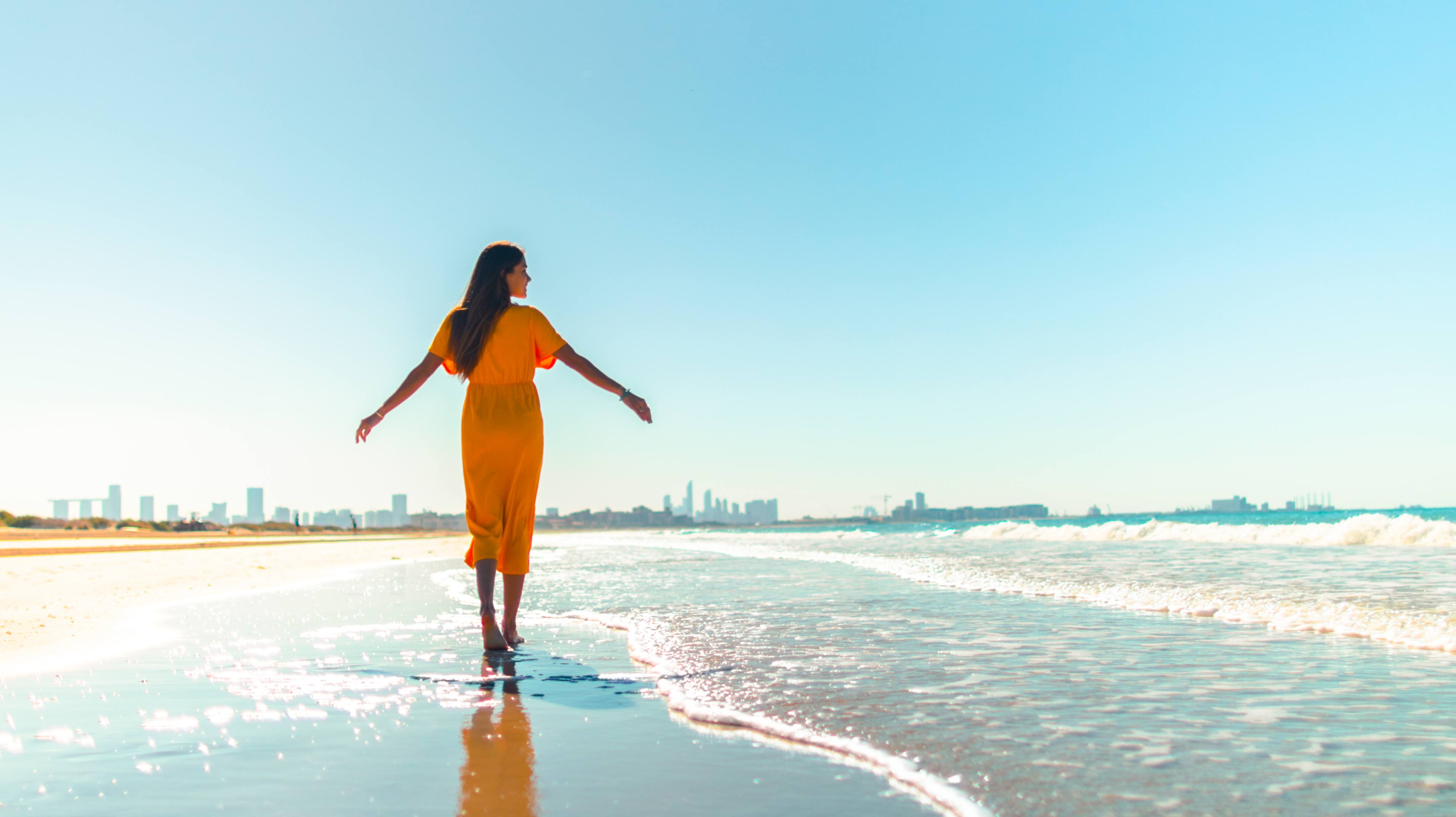 Woman wearing an orange dress and walking on the beach