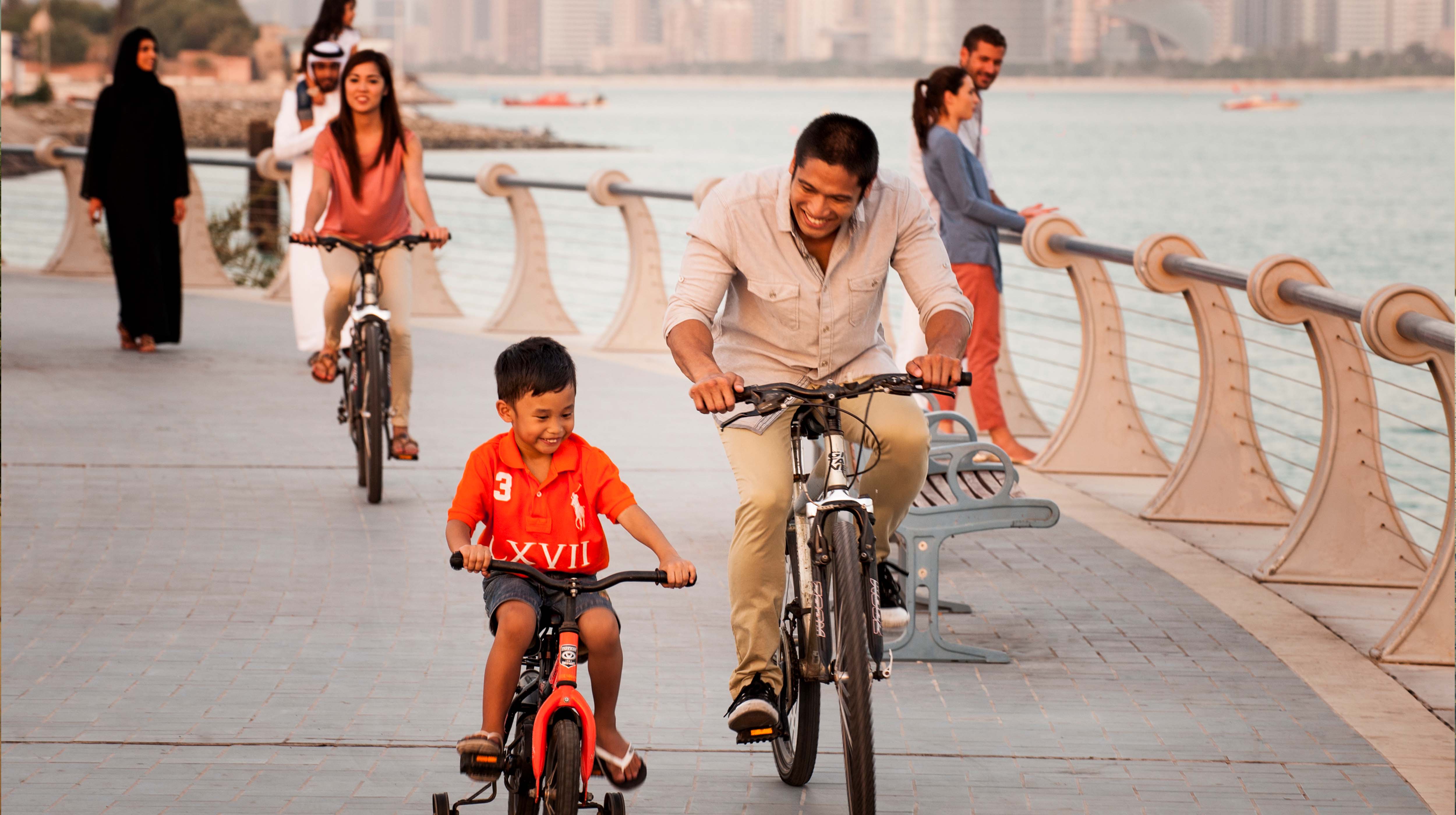 رجل وابنه يستمتعان بركوب الدراجات الهوائية في ممشى بإحدى كورنيشات أبوظبي