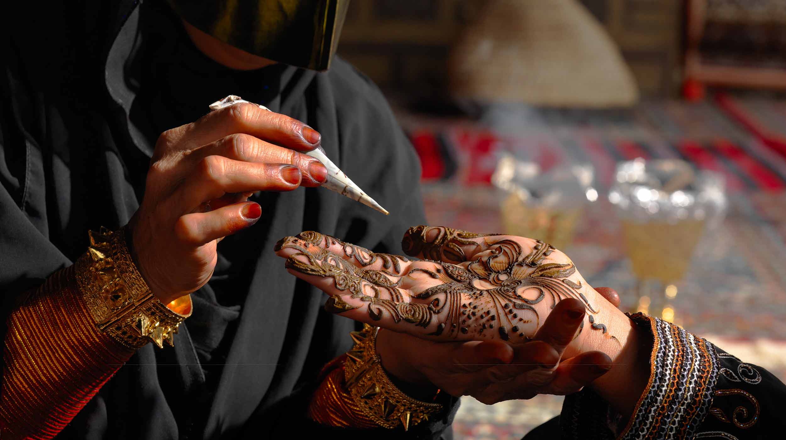 Due mani da donne. L’una fa un henné alla mano dell’altra donna.