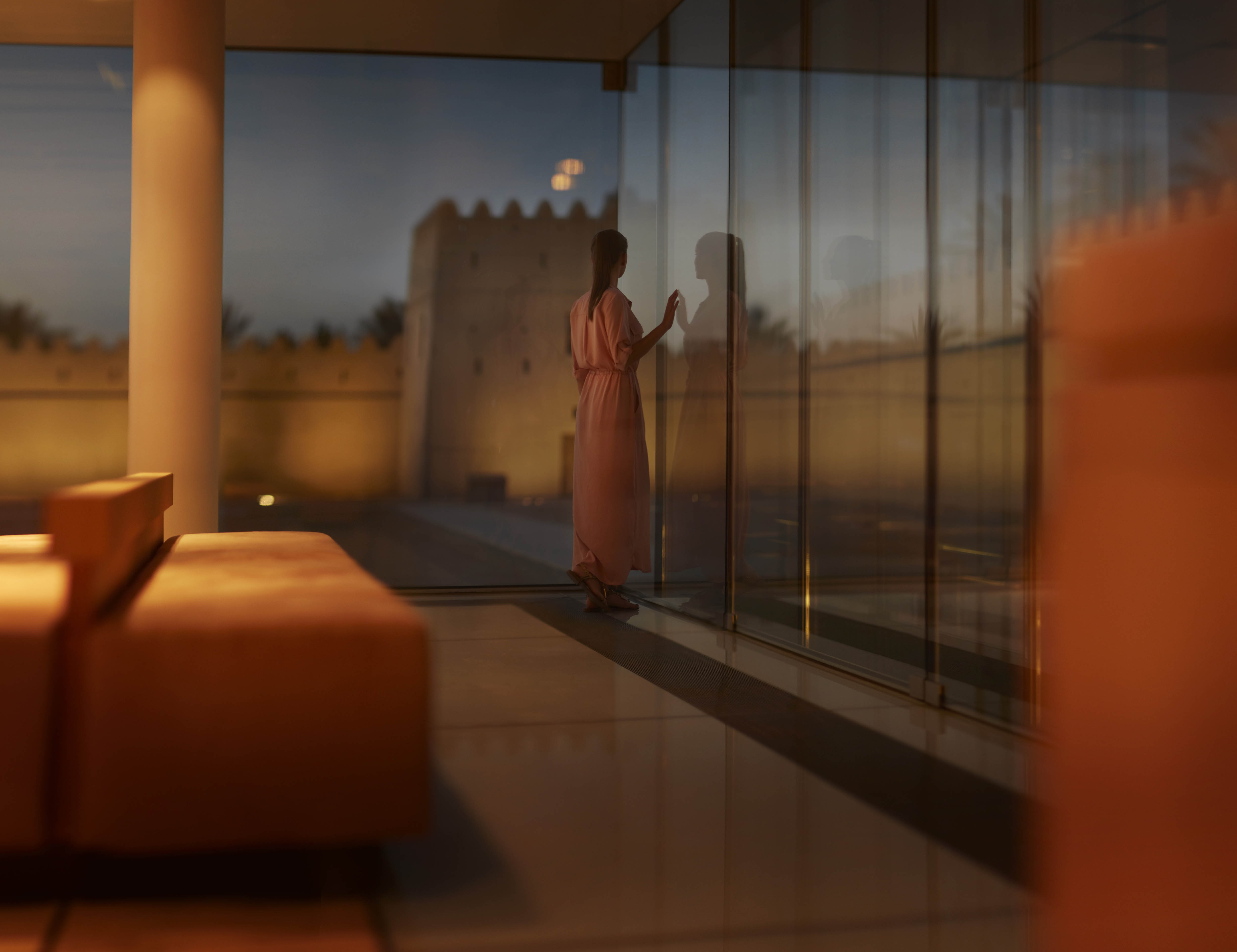 Western woman standing in front of a glass wall near a fort in the Emirate of Abu Dhabi