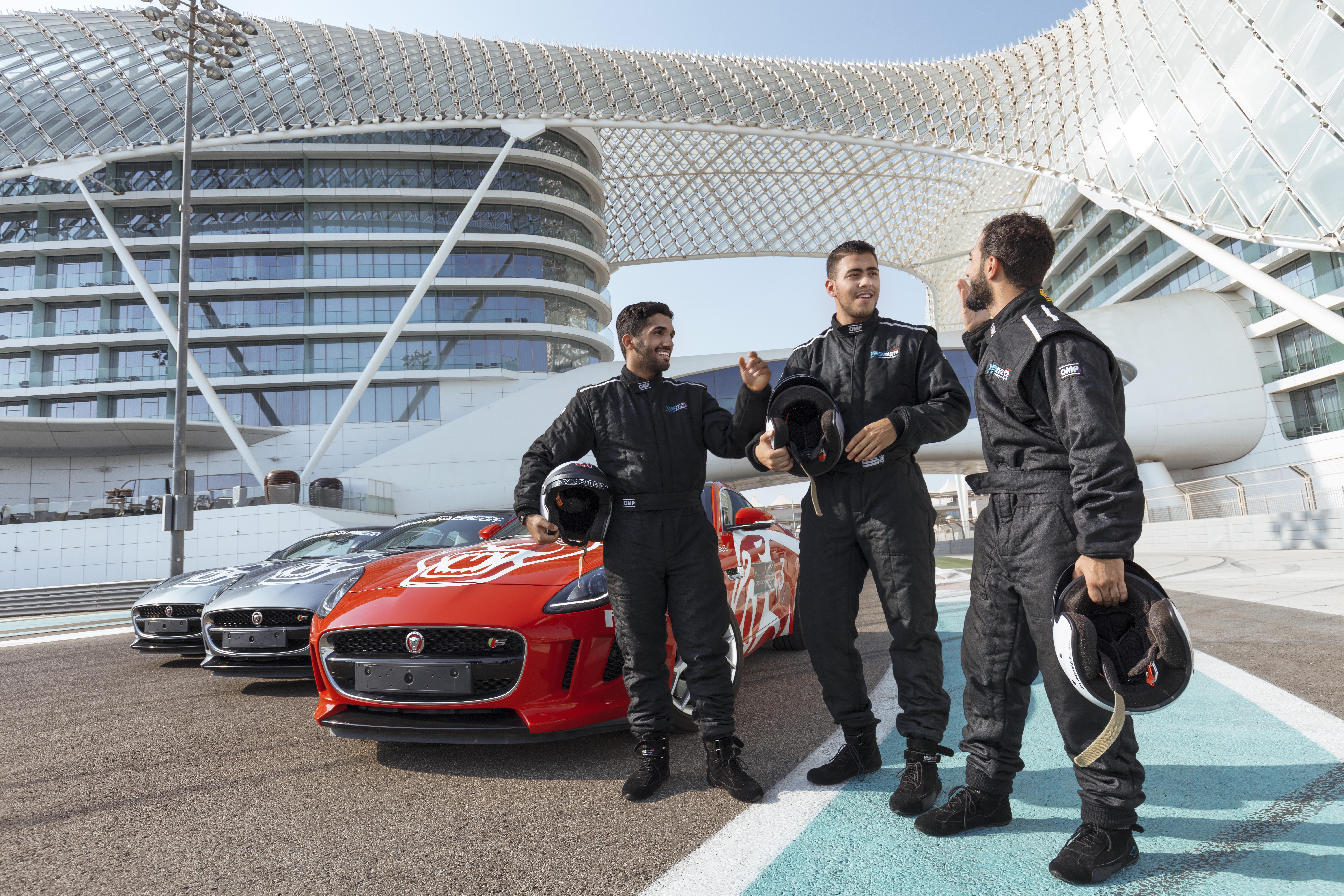 Трое молодых мужчин в гоночной форме смотрят на перед машинами на гоночной трассе в Абу-Даби